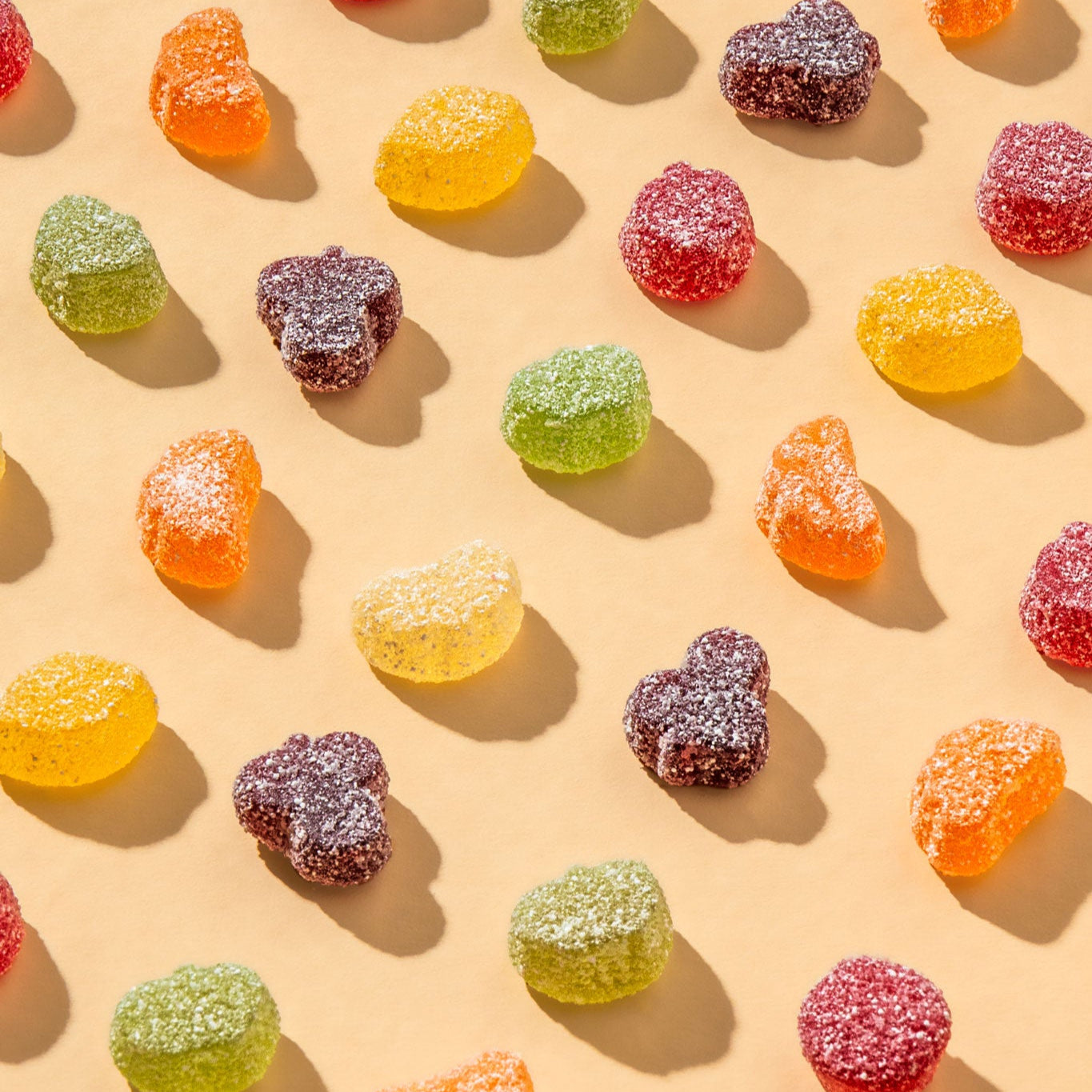 Einzelne Happy Sour Bio-Fruchtgummi in angeordnet auf einem beigen Grund mit Schattenspielen.