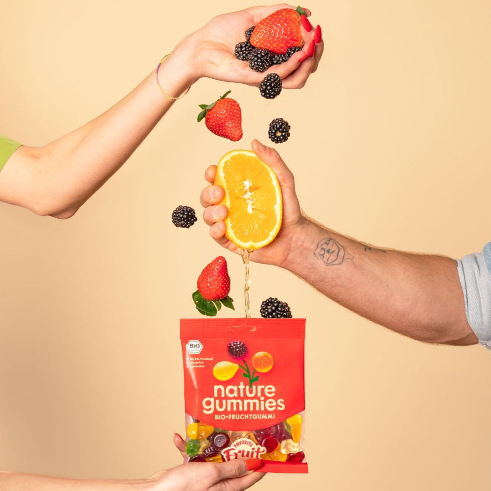 Hände pressen Saft aus Bio-Früchten in nature gummies Favorite Fruit Packung.