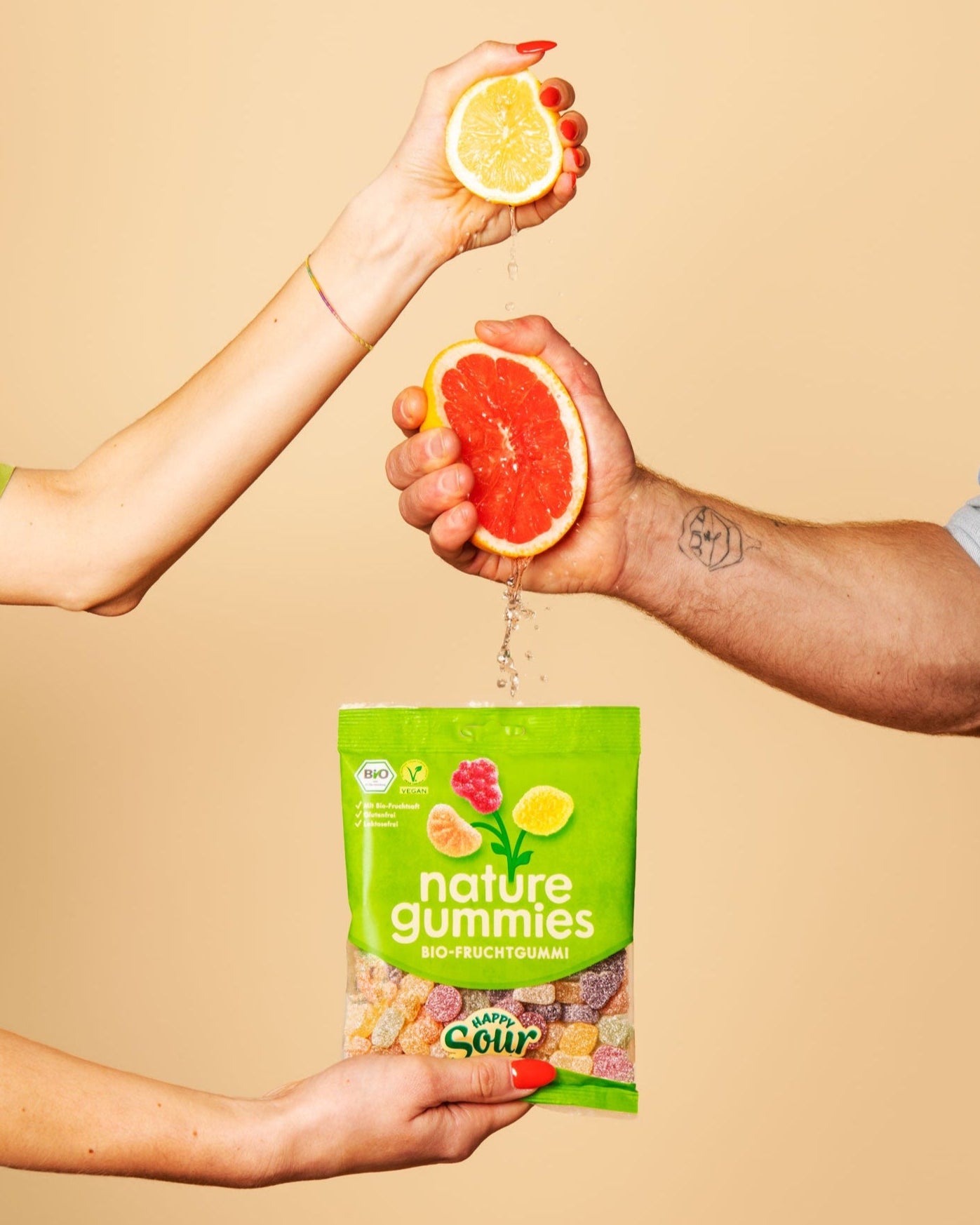 Hände pressen Saft aus Bio-Früchten in nature gummies Happy Sour Packung.
