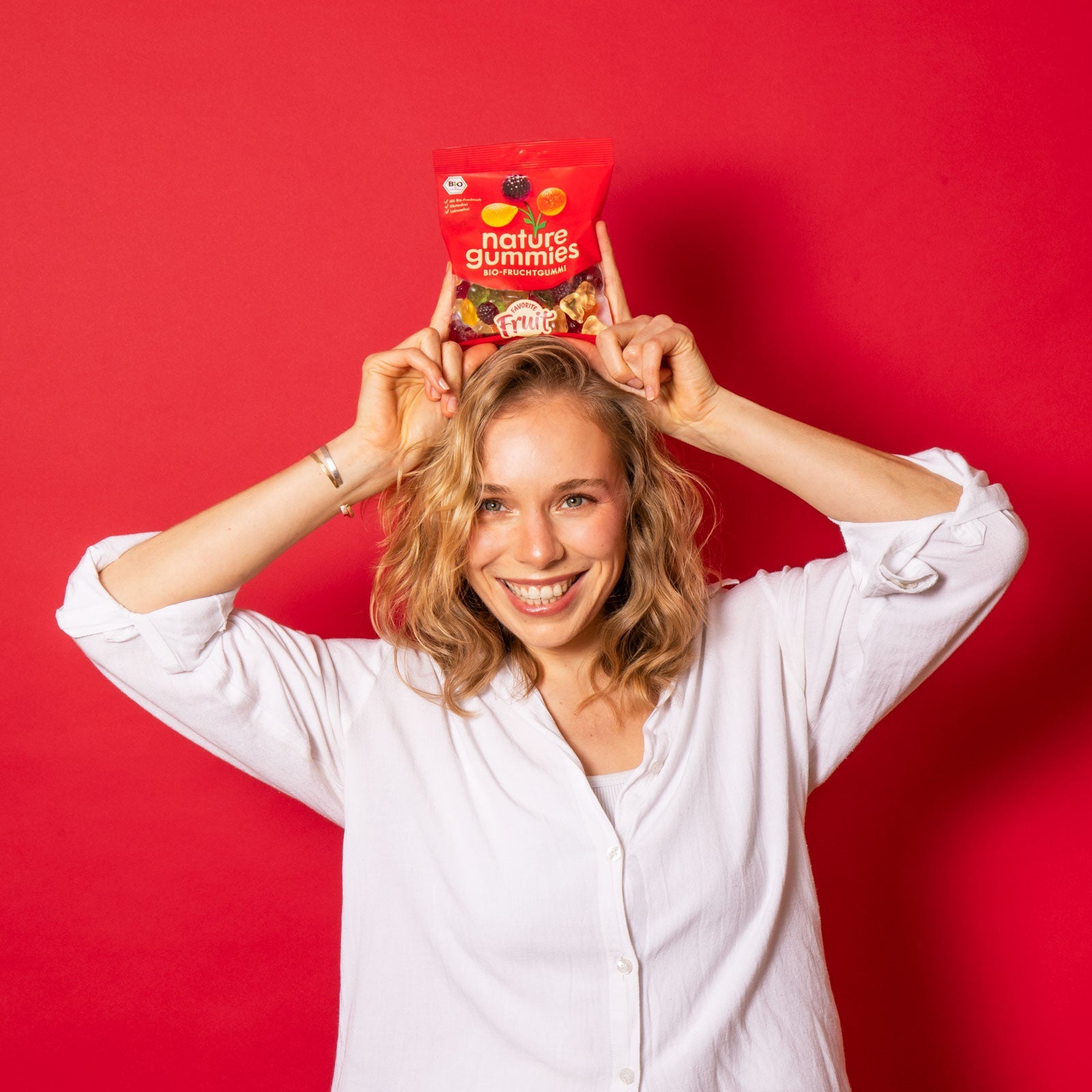 Eine blonde Frau hält eine nature gummies Packung der Sorte Favorite Fruit freudig und verspielt über ihrem Kopf. 