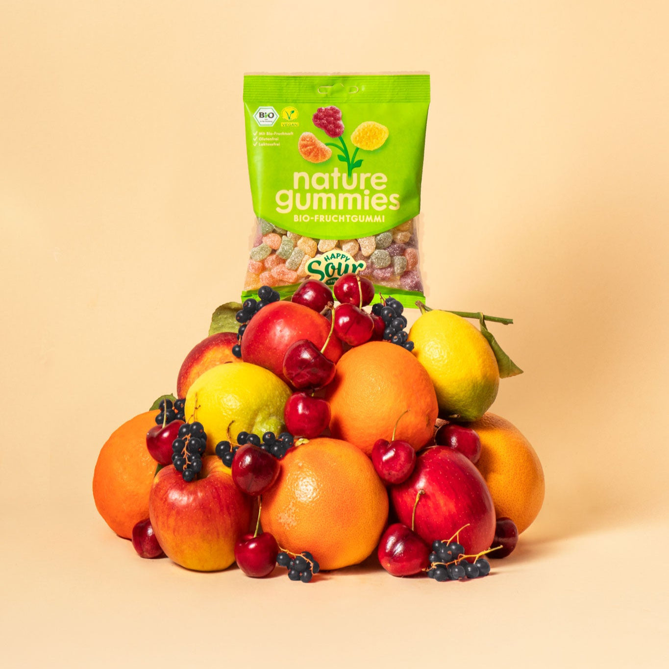 nature gummies Happy Sour Bio-Fruchtgummis auf einem Berg aus Früchten – Apfel, Orange, schwarze Johannisbeere, Kirsche, Grapefuit und Zitrone.