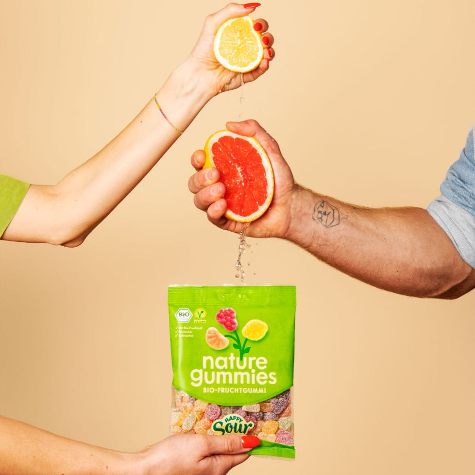Hände pressen Saft aus Bio-Früchten in nature gummies Happy Sour Packung. 