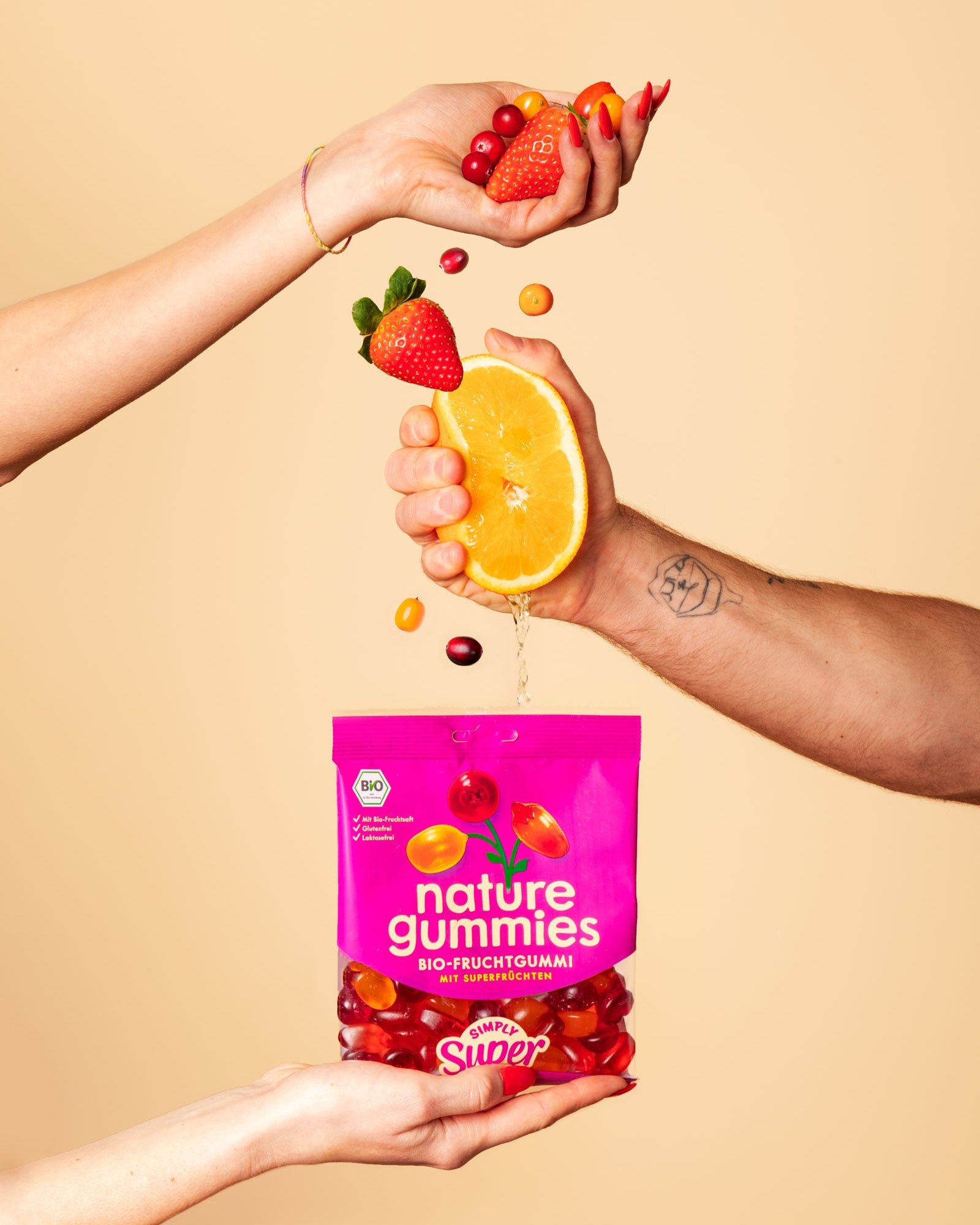 Hände pressen Saft aus Bio-Früchten in nature gummies Simply Super Packung. 